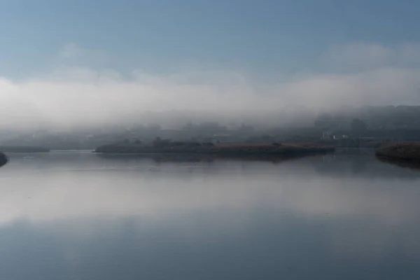 Fog river landscape at sunrise with low clouds and reflection on the water in Alcacer do Sal, Portugal