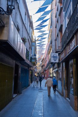 İspanya 'da, Badajoz' da gezen turistler güzel, renkli kare bayraklı binalarla güzel bir caddede yürüyorlar.