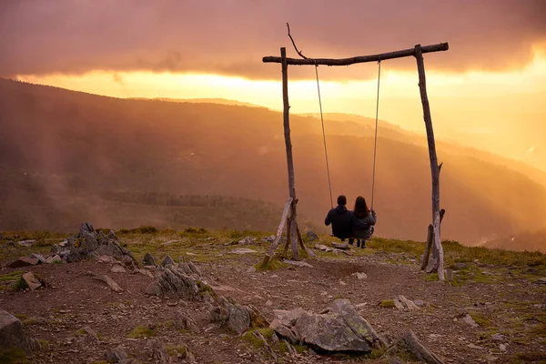 Romantik çift sosyal mesafeler Lousa Dağı, Portekiz 'de gün batımında salıncakta sallanıyor.