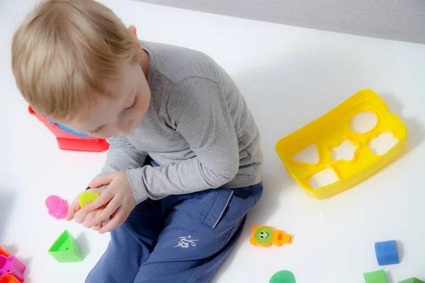 Niño pequeño de tres años se sienta en la mesa y juega con plas —  Fotos de Stock