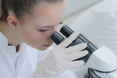 Genç bayan bilim adamı mikroskopla bir çalışmanın içine bakıyor.