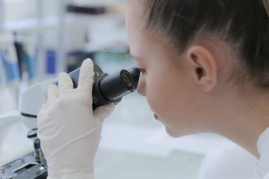 Genç bayan bilim adamı mikroskopla bir çalışmanın içine bakıyor.