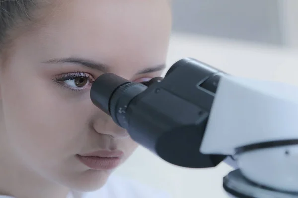 Jeune femme scientifique regardant à travers un microscope dans un laboratoire — Photo