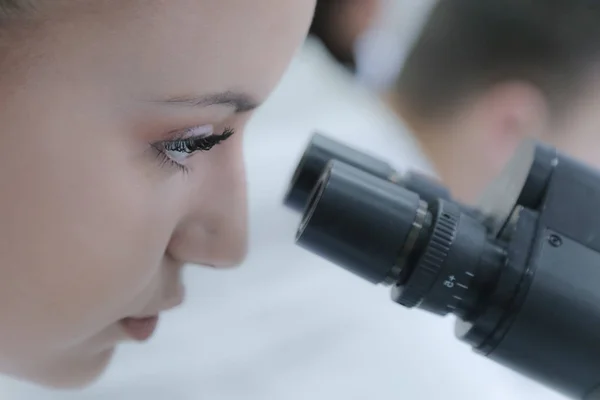 Jeune femme scientifique regardant à travers un microscope dans un laboratoire — Photo