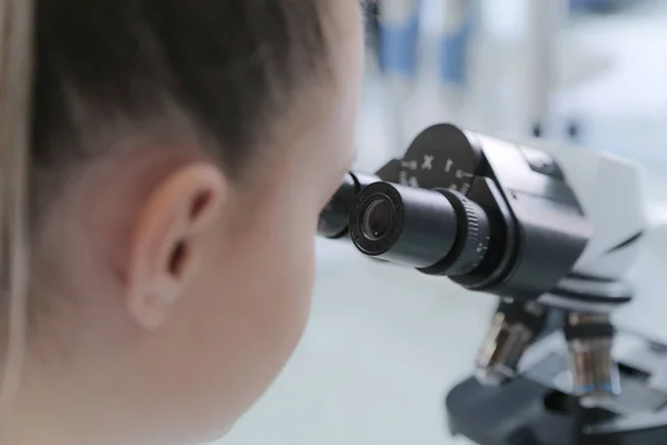 Joven científica mirando a través de un microscopio en un laboratorio — Foto de Stock