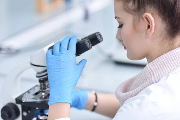 Νεαρή γυναίκα επιστήμονας κοιτάζοντας μέσα από ένα μικροσκόπιο σε ένα εργαστήριο — Φωτογραφία Αρχείου
