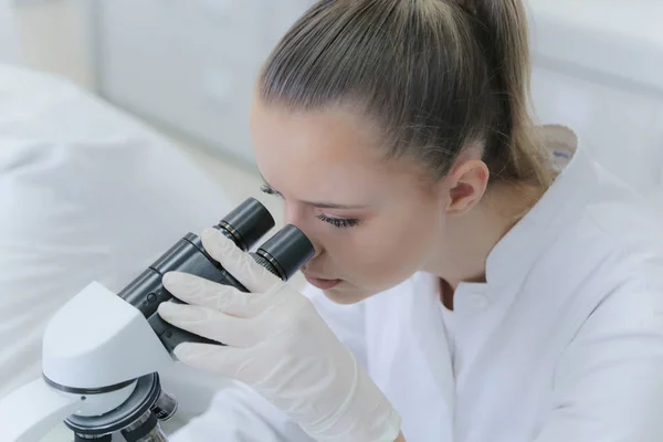 Joven científica mirando a través de un microscopio en un laboratorio — Foto de Stock