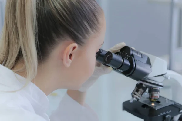 Νεαρή γυναίκα επιστήμονας κοιτάζοντας μέσα από ένα μικροσκόπιο σε ένα εργαστήριο — Φωτογραφία Αρχείου