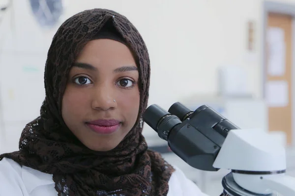 Joven científica musulmana africana que mira a través de un microsco —  Fotos de Stock