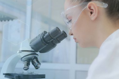 Genç bayan bilim adamı mikroskopla bir çalışmanın içine bakıyor.