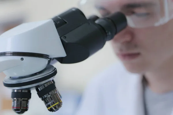 Joven científico masculino mirando a través de un microscopio en un laboratorio — Foto de Stock