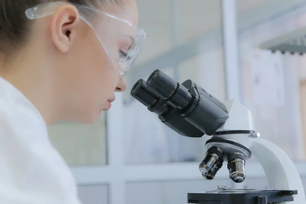 年轻的女科学家在实验室的显微镜下观察 — 图库照片