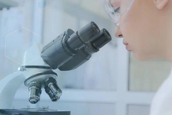 Молода жінка-вчена, яка дивиться через мікроскоп у лабораторії — стокове фото