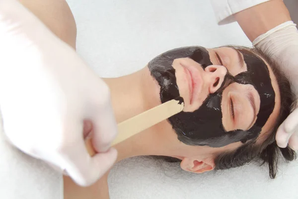 Jonge mooie vrouw die zwarte houtskool gezichtsmasker aanbrengt. Huid — Stockfoto