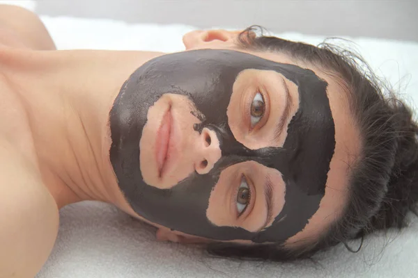 Young beautiful woman applying black charcoal facial mask. Skin