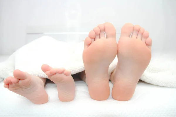 Madre e hijo pequeño acostados en la cama, sus pies en el foco —  Fotos de Stock