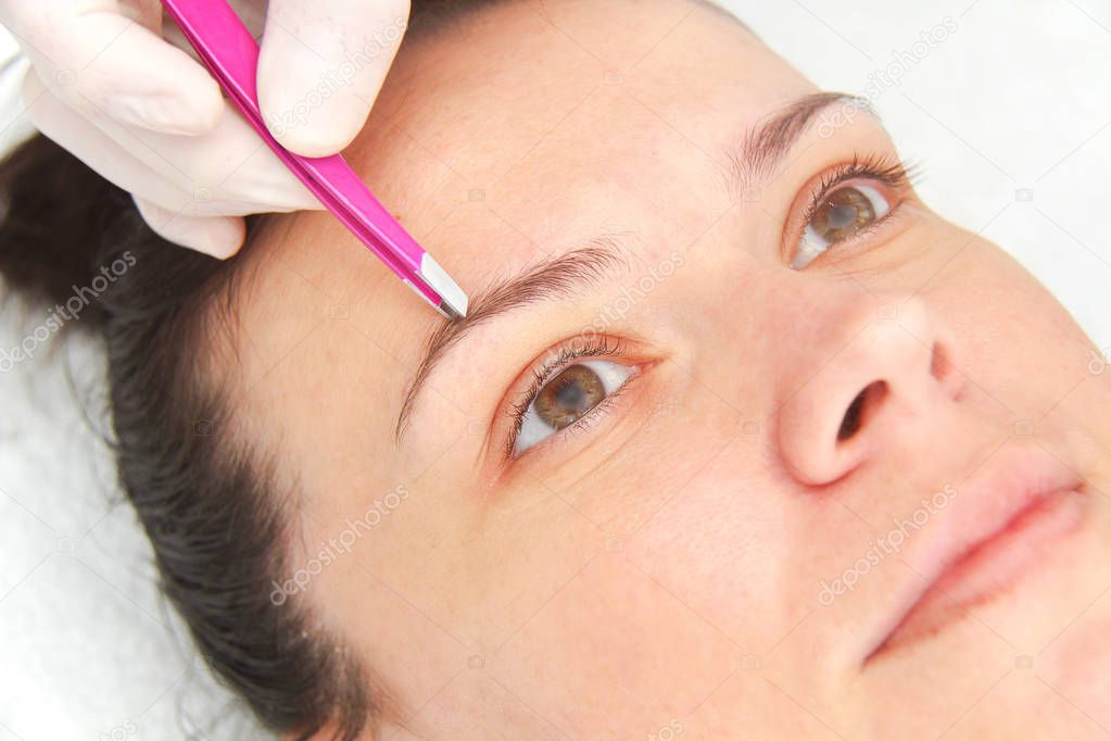 Young woman having professional eyebrow correction procedure in 