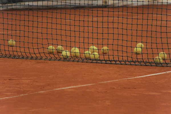 Palle da tennis su campo rosso con rete grigia — Foto Stock