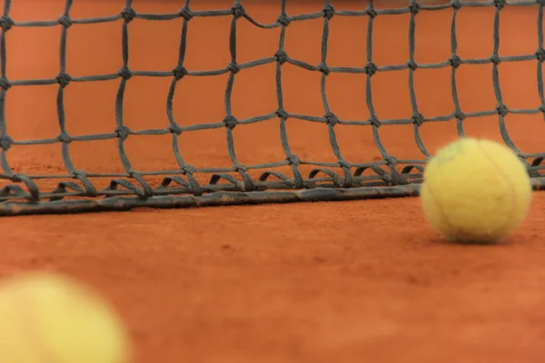 Tennisbälle auf rotem Platz mit grauem Netz — Stockfoto