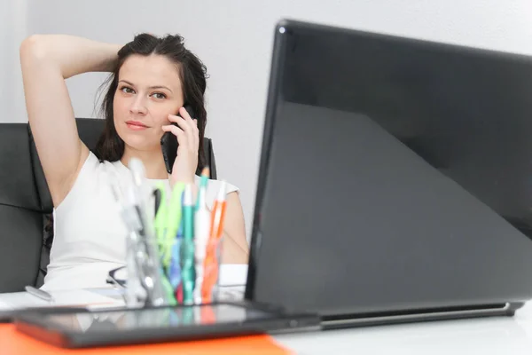 Atractiva mujer de negocios usar el teléfono inteligente y sentarse en su varita —  Fotos de Stock