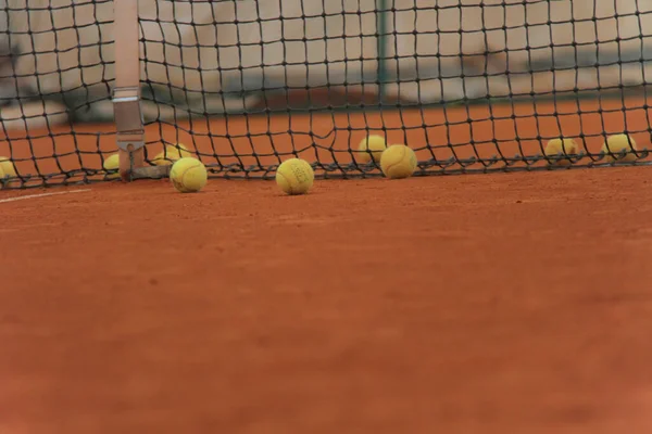 Pelotas de tenis en pista roja con red gris —  Fotos de Stock