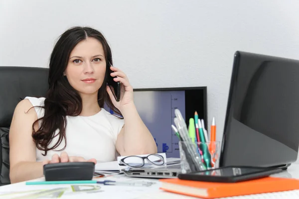 Atractiva mujer de negocios usar el teléfono inteligente y sentarse en su varita —  Fotos de Stock