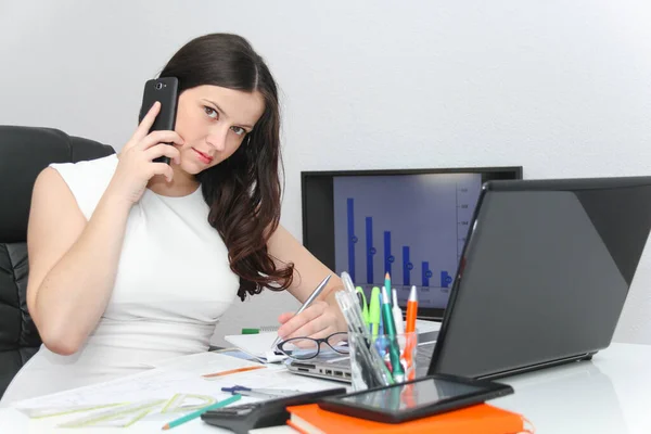 Atractiva mujer de negocios usar el teléfono inteligente y sentarse en su varita —  Fotos de Stock