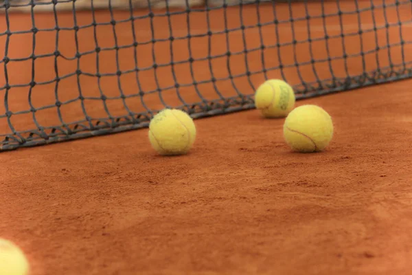 Pelotas de tenis en pista roja con red gris —  Fotos de Stock