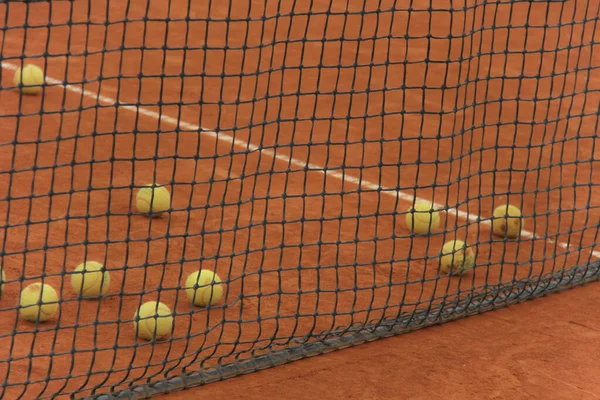 Pelotas de tenis en pista roja con red gris — Foto de Stock