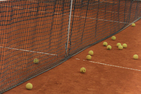 Tennis balls on red court with gray net