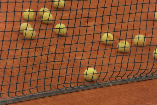 Tennisbollar på röd bana med grått nät — Stockfoto