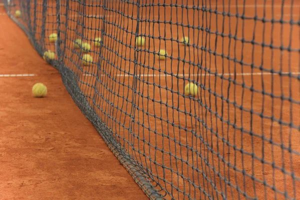 Pelotas de tenis en pista roja con red gris — Foto de Stock