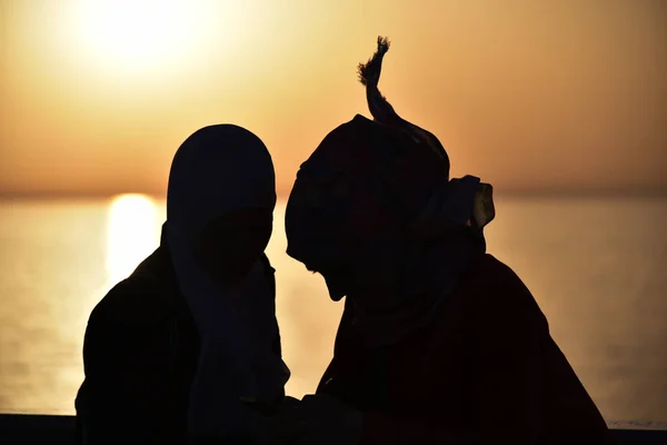 Achteraanzicht van twee jonge vrouwen kijken naar zee bij zonsondergang op de zee — Stockfoto