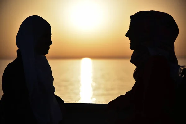 Vista trasera de dos mujeres jóvenes mirando al mar al atardecer en el mar — Foto de Stock