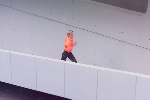 Ung kvindelig løber i hættetræner i byen street.Fit krop - Stock-foto