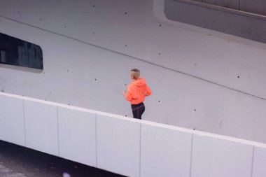 Kapüşonlu genç bayan koşucu şehir sokaklarında koşuyor. Formda vücut sıkı çalışma gerektirir. Şehir sporu konsepti. Spor kıyafetleriyle egzersiz yapan genç bir bayan..