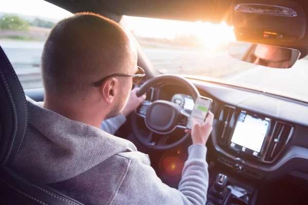 Hombre mirando el teléfono móvil mientras conduce un coche . — Foto de Stock