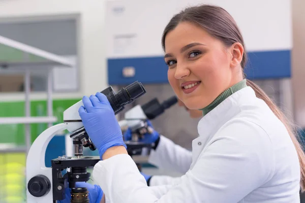 Jonge vrouwelijke wetenschapper kijkt door een microscoop in een laboratorium — Stockfoto