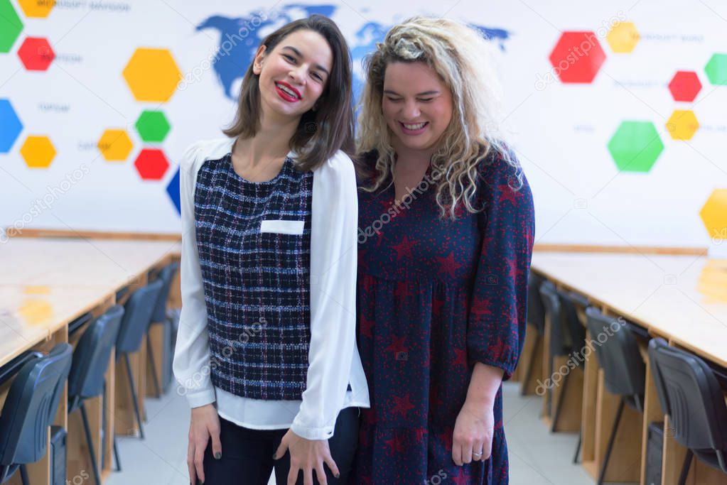 Two college students standing inside classroom and chatting afte