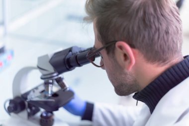 Genç bilim adamı bir laboratuarda mikroskoptan bakıyor.