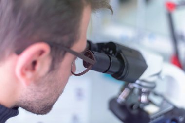 Genç bilim adamı bir laboratuarda mikroskoptan bakıyor.