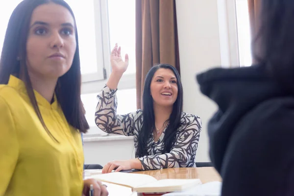 Vista frontale di studentessa seduta in classe e sollevando ha — Foto Stock