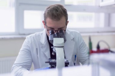Genç bilim adamı bir laboratuarda mikroskoptan bakıyor.