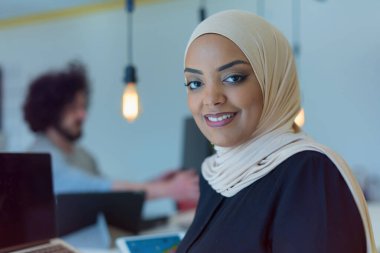 Genç Afrikalı Amerikalı iş kadını ayakta ve gülümsüyor. Ekibi arka plandayken başarılı bir iş adamı pozu verdi..