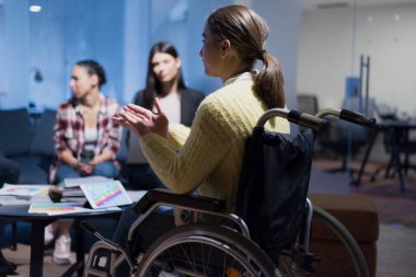 İş arkadaşları ofiste çalışan engelli genç bir kadın. O, iş akışı hakkında gülümsüyor ve tutkulu. Ortak çalışma alanında performans sergilemek. Ofisteki insanlar birlikte çalışıyor..