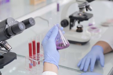 Laboratuvarda test tüpleri ve mikroskop ile çalışan iki genç laboratuvar bilim adamı klinik laboratuarında test veya araştırma yapıyor. Bilim, kimya, biyoloji, tıp ve insan konsepti.