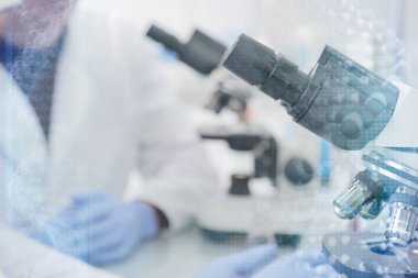 Laboratuvarda test tüpleri ve mikroskop ile çalışan iki genç laboratuvar bilim adamı klinik laboratuarında test veya araştırma yapıyor. Bilim, kimya, biyoloji, tıp ve insan konsepti.