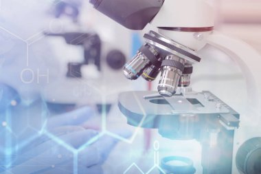 Laboratuvarda test tüpleri ve mikroskop ile çalışan iki genç laboratuvar bilim adamı klinik laboratuarında test veya araştırma yapıyor. Bilim, kimya, biyoloji, tıp ve insan konsepti.