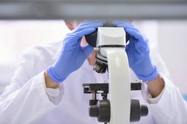 Laboratuvarda mikroskopla araştırma, mikrobiyolojik analiz ve tıp yapan genç bir bilim adamı..