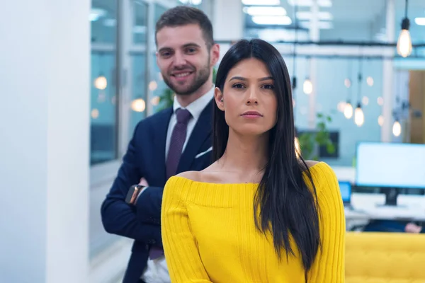 Portrait of two young co workers standing at workplace inside modern co working space.